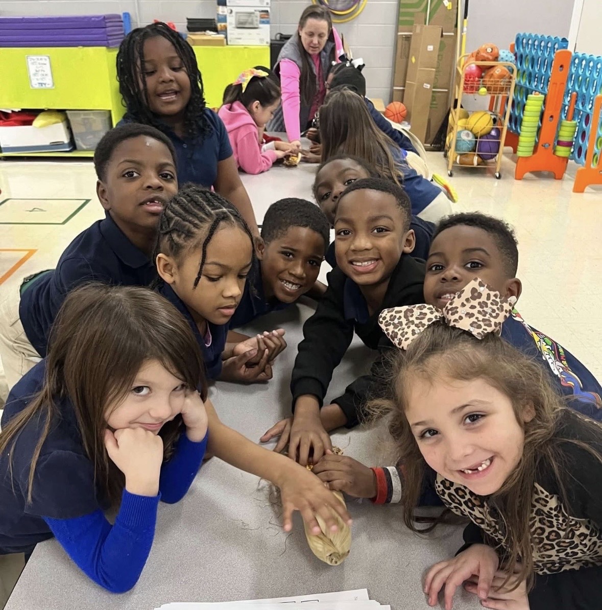 Children gathered around a table working on a hands-on classroom activity with a small object.